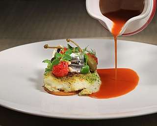 Un piatto gourmet con pesce, verdure e salsa rossa.